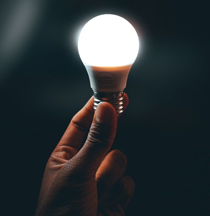 A close-up of a hand holding a bright LED light bulb against a dark background.